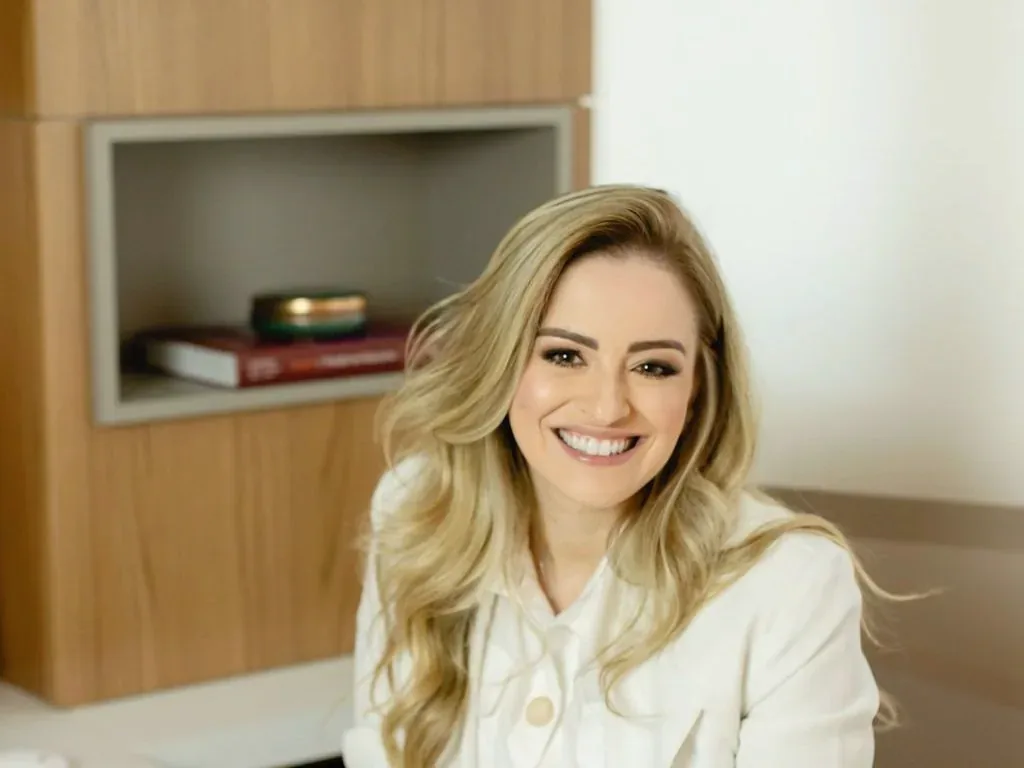 Dra. Maria Isabel sorrindo, sentada à mesa do consultório
